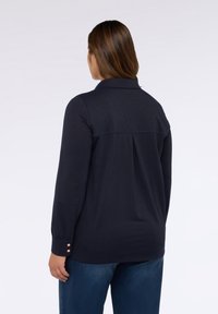Blusa de manga larga de color marino con cuello camisero, pliegue trasero y botones decorativos en los puños. Confeccionada con una tela suave para mayor confort.