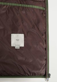 Intérieur de veste marron avec bordure verte, fermeture éclair visible et étiquette blanche indiquant MNG Man, fabriqué au Vietnam, déperlant, taille moyenne.