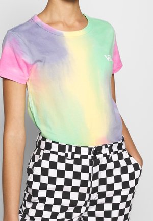 Person iført en pastel tie-dye t-shirt med Vans-logo, parret med høj taljede sort-hvide ternede bukser, hænderne i lommerne.