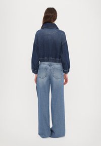 Denim jaka ar saīsinātu piegriezumu, tumši zila krāsa, elastīga vidukļa daļa un liels apkakle. Kombinēta ar gaiši ziliem, platu kāju džinsiem.