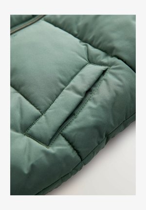 Grüne, gesteppte Puffjacke aus einem Material mit glatter Textur, das eine Klappentasche und kontrastierende Nähte auf der Oberfläche aufweist.