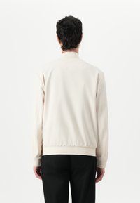 Light beige bomber jacket with a smooth texture, elastic cuffs, and hem. Features a classic collar and ribbed detailing. Back view shown.