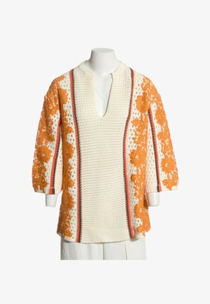 Lange crèmekleurige gebreide trui met diepe V-hals, oranje bloemen kantpanelen en verticale rode en bruine strepen op mouwen en voorkant.