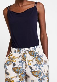 Top senza maniche blu navy con scollo drappeggiato, abbinato a pantaloni crema con un motivo paisley blu e oro e una vita elastica.