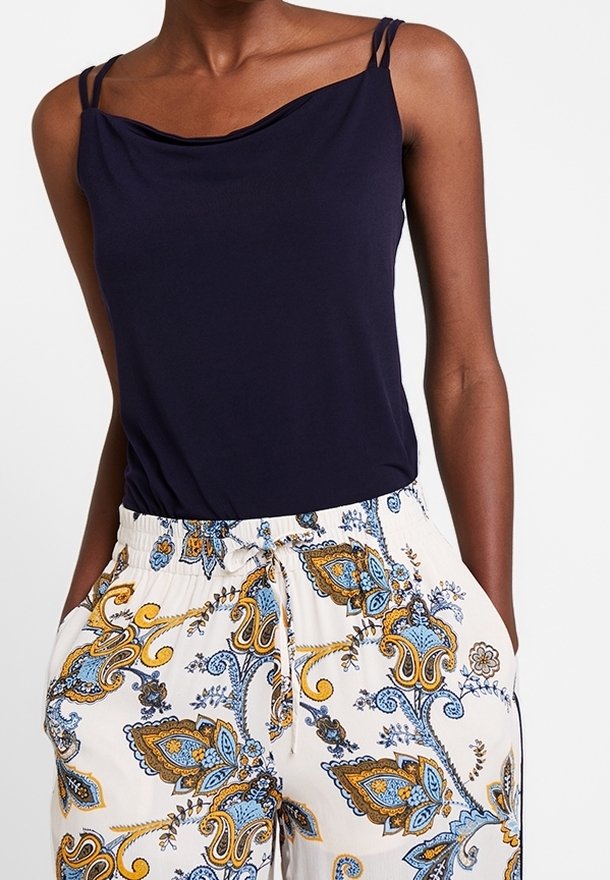 Top senza maniche blu navy con scollo drappeggiato, abbinato a pantaloni crema con un motivo paisley blu e oro e una vita elastica.