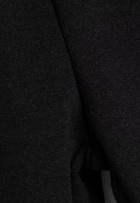 Schwarzer Strickstoff mit weicher Textur, der ein gefaltetes Design und ein Bindedetail auf der linken Seite aufweist, was seine schlichte Eleganz unterstreicht.