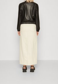 Sort læder bomberjakke med elastisk talje og cuffs, parret med en cremefarvet, lang, lige denimnederdel og chunky hæle sandaler.