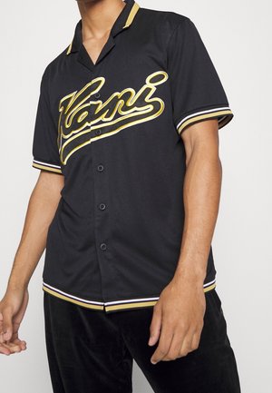 Camicia nera a maniche corte con bottoni, decorata con dettagli dorati e bianchi, caratterizzata da un logo in corsivo e colletto e polsini a righe. Tessuto morbido e leggero.