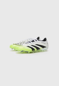 Botas de fútbol blancas y negras con una parte superior texturizada, acentos verdes y tacos transparentes. Presenta tres rayas negras y un logo.