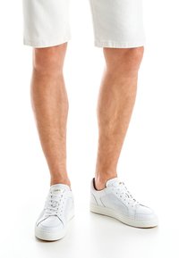 Weiße Leder-Sneaker mit glatter Textur, ausgestattet mit Schnürsenkeln, Seitenpanelen und einem gepolsterten Kragen. Die Sohle ist flach und langlebig.