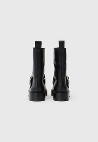 Μαύρες δερμάτινες μποτές μέχρι τον αστράγαλο με λεία επιφάνεια, στρογγυλεμένες μύτες και έντονες πλαινές αγκράφες. Διαθέτουν κορδόνια για εύκολη χρήση και χοντρή σόλα.