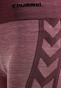 Bordowe legginsy sportowe z teksturowanym wykończeniem, z czarnym logo "hummel" oraz kontrastowym ciemnym wzorem w zygzak na boku.