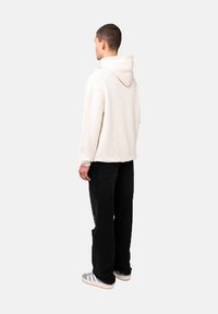 Felpa crema con cappuccio grande, vestibilità comoda e polsini a costine, abbinata a pantaloni neri e sneakers grigie a righe. Design minimalista.