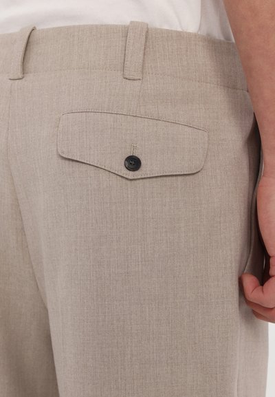 Shorts ajustés beige clair en tissu texturé, avec une poche arrière dotée d'un bouton noir et des passants de ceinture.