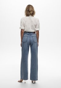 Vit broderad blus med korta ärmar, matchad med högmidjade, vida ljusblå denimjeans. Klara klackar synliga längst ner.