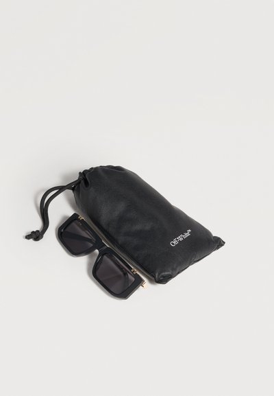 Lunettes de soleil rectangulaires noires à côté d'une pochette noire à cordon avec le logo « Off-White » sur un fond clair.