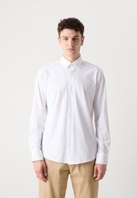 Hvit langermet skjorte laget av glatt stoff, med knapp-ned krage og full front med knapper. Pyntet med enkle mansjetter.