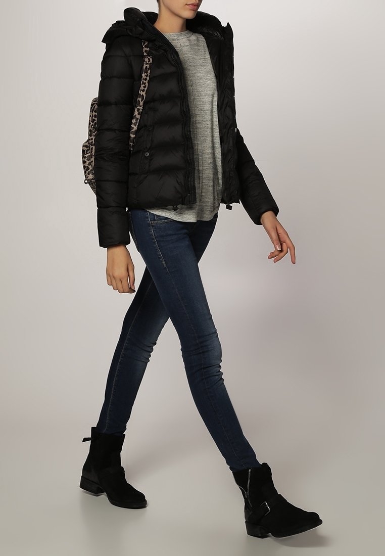 Schwarze Puffjacke mit Kapuze, grauer Pullover, blaue Skinny Jeans und schwarze Stiefel bis zum Knöchel. Rucksack mit Leopardenmuster-Trägern.