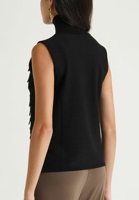 Top noir sans manches avec un col montant, présentant des volants texturés sur les côtés, fabriqué en matériau doux et extensible.