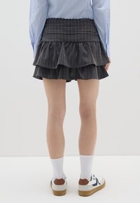 Zwarte gestreepte rok met tiered ruches, met een smock tailleband. In combinatie met witte sokken en sneakers met bruine accenten.