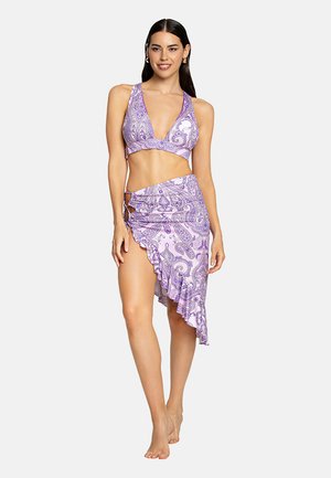 Bikini viola con motivo paisley e scollatura profonda, abbinato a una gonna avvolgente con orlo arricciato e legatura laterale. Texture del tessuto liscia.