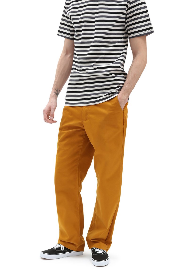 T-shirt rayé noir et blanc associé à un pantalon ample jaune moutarde et des baskets noires. Matériaux en coton, design décontracté, poches latérales.