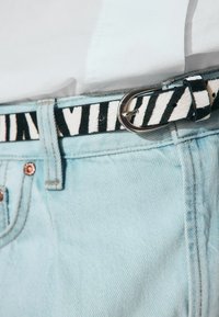 Jean en denim bleu clair avec une ceinture en tissu rayé noir et blanc dotée d'une boucle en argent, mettant en avant la texture et le contraste.