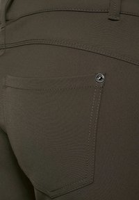 Gros plan sur la poche arrière d'un pantalon vert olive foncé avec des coutures visibles et un rivet métallique près du coin de la poche.