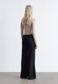 Long-sleeve cream top with fitted bodice paired with high-waisted black wide-leg trousers. Smooth texture, neutral colors, minimal design.