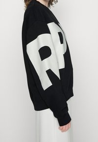 Sudadera negra de mezcla de algod�ón, con un gran gráfico blanco en el frente. Tiene un cuello redondo y puños acanalados.