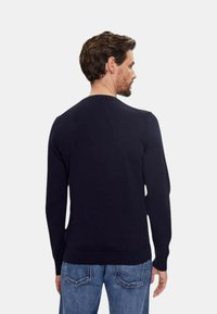 Marineblauwe gebreide trui met lange mouwen, geribde manchetten en zoom, ontwerp met ronde hals, van achteren zichtbaar, gecombineerd met lichtblauwe jeans.