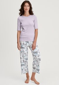 Haut léger lilas à manches courtes associé à un pantalon de pyjama blanc arborant un motif coloré inspiré du voyage, avec des monuments et des illustrations.
