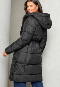 Melnas pūkumu jaka ar noņemamu kapuci, quilted dizainu, jostu jostasvietā un sānu kabatām ar pogu aizdares.