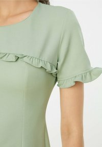 Kortärmad klänning i ljusgrön tyg med rynkade detaljer längs halsringningen och ärmarna. Slät textur, figursydd form.