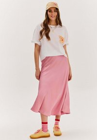 Bílý krátký rukáv tričko s potiskem kapsy, spárované s růžovou saténovou sukní, žlutými teniskami a růžovo-červenými pruhovanými ponožkami.