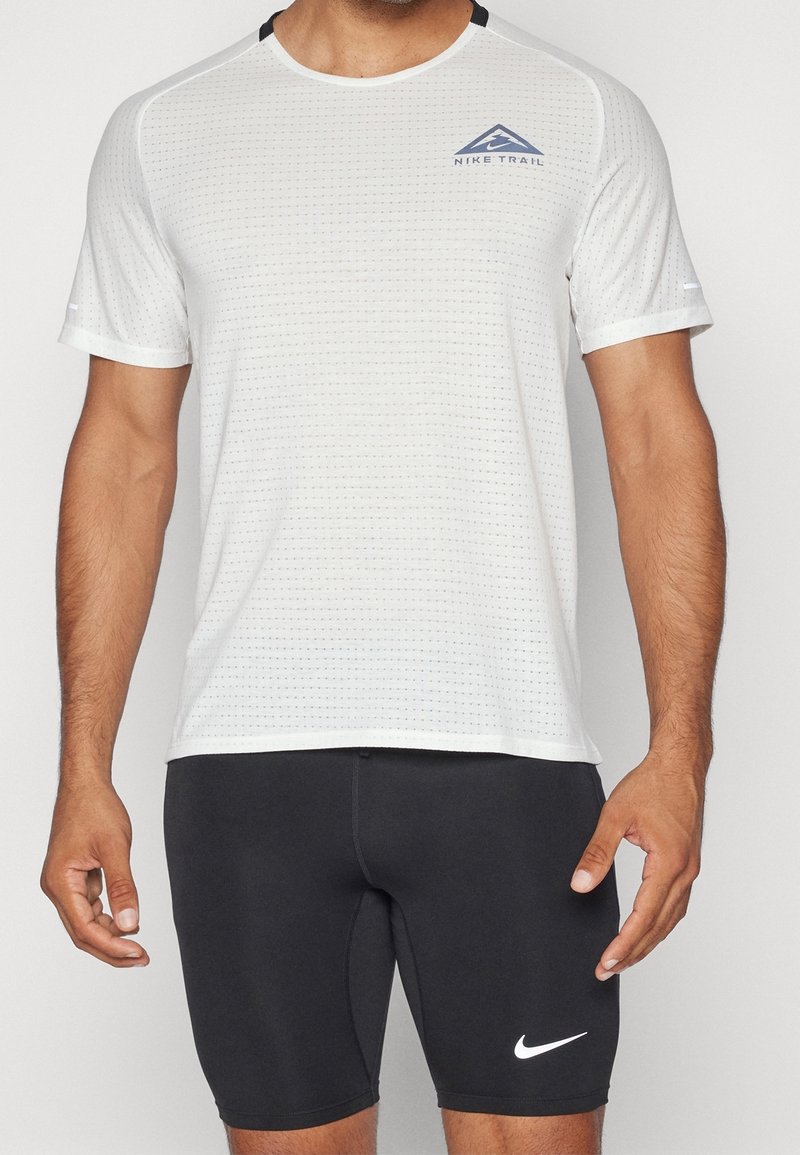 Vitt sportt-shirt med en texturerad mönster, med en blå logotyp och svarta detaljer. Matchas med svarta åtsittande shorts med en vit logotyp.