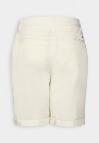Shorts ajustés blanc cassé avec passants de ceinture, ourlets retroussés et deux poches passepoilées arrière, vus de dos sur un fond uni.