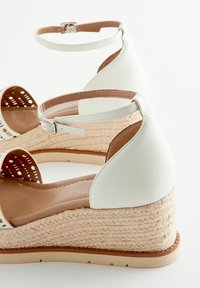 Wedges de espadrille blancos con un tacón de yute texturizado, una correa en el tobillo y detalles recortados en la parte delantera. Forro interno suave.
