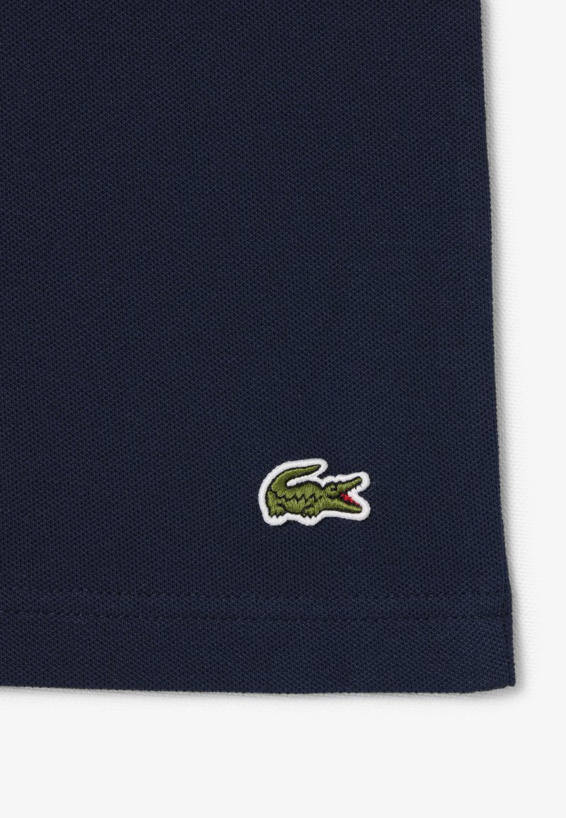 Tissu texturé bleu marine avec un petit logo crocodile vert brodé près de l'ourlet en bas à droite.