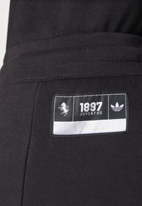 Čierne atletické nohavice s textúrovanou tkaninou, s vyšitou etiketou s logom "1897 JUVENTUS" a bielym emblémom Adidas.
