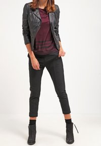 Schwarze Lederbikerjacke über einem burgunderfarbenen Hemd mit drei horizontalen Streifen, kombiniert mit schwarzen 7/8-Hosen und Stiefeletten.