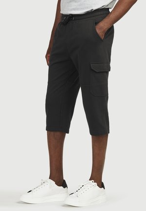 Sorte cargo shorts lavet af et glat stof, med sidelommer, snor i taljen og knælængde. Båret med hvide sneakers.