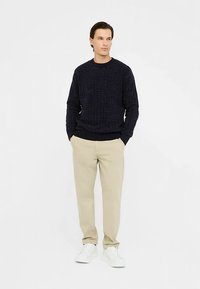 Marineblauwe gebreide trui met structuur en een ronde hals, gecombineerd met beige getailleerde broek en witte vetersneakers.