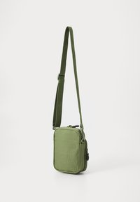 Borsa a tracolla di stoffa verde con forma rettangolare, chiusura con zip, tracolla regolabile e superficie liscia. Presenta una piccola tasca laterale.
