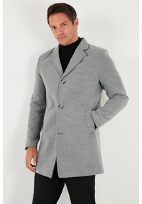 Abrigo gris de mezcla de lana con cuello estructurado, dos botones, bolsillos laterales y un bolsillo en el pecho. Textura suave y corte ajustado.