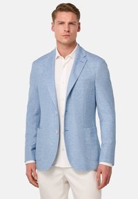 Blazer azul claro hecho de un tejido texturizado, con un diseño de un solo botón, solapas en pico y dos bolsillos frontales, llevado sobre una camisa blanca.