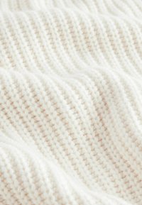 Cremefarbener, gestrickter Stoff mit einem strukturierten Muster aus erhöhten Stichen und sanften Wellen, der ein weiches und gemütliches Erscheinungsbild aufweist.