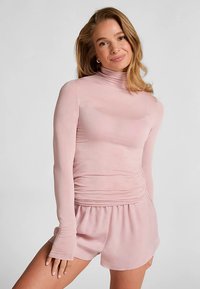 Lichtroze top met lange mouwen, hoge hals en plooidetail bij de taille, gecombineerd met bijpassende shorts in losse pasvorm. Zacht, gladde stof.