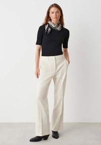 Top nero a coste a maniche corte, pantaloni crema a gamba larga e stivaletti neri con tacco. Include una sciarpa a righe in bianco e nero annodata al collo.