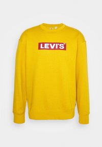Gelbes Sweatshirt mit langen Ärmeln, das ein rotes rechteckiges Levi's-Logo auf der Vorderseite hat. Hergestellt aus weichem Stoff mit gerippten Bündchen.